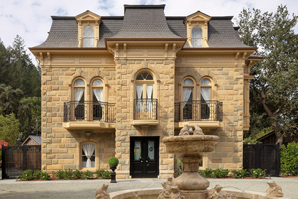 Historic French Second Empire stone mansion with dormer windows and a decorative fountain on the front lawn.