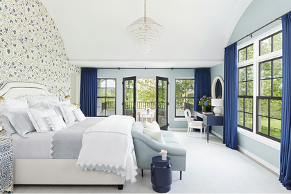 Spacious master bedroom with light blue walls, floral wallpaper accent wall, white bed, navy drapes, and large windows leading to a balcony.