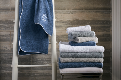 Blue textured bath towel hanging on a wooden ladder next to a neatly folded stack of grey and white towels.