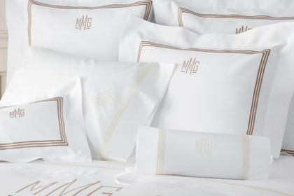 White monogrammed bedding set with matching pillows and a pillowcase, featuring gold embroidered borders and the initials 'MMG' on a white background.