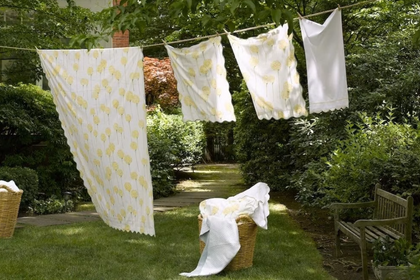 White and patterned bed sheets hanging outdoors on a clothesline in a lush green backyard garden setting.