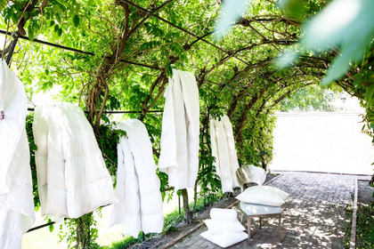 White bed sheets and linens hanging on a clothesline outdoors surrounded by green foliage.
