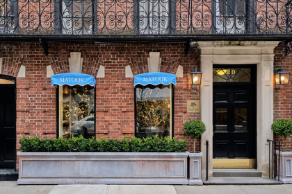 Exterior storefront with a red brick facade, blue window awnings, window flower boxes, and a black entryway door.