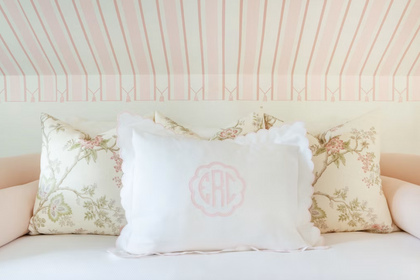 Close-up of a blush pink daybed styled with fluffy white pillows and floral throw cushions against a painted wood paneled wall.