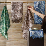 Hand reaching for Balthazar marbled napkins in green, brown and blue.