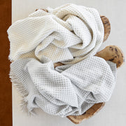 Overhead view of ivory and light gray Cleo knit throws with fringe, draped in a live-edge wood bowl.