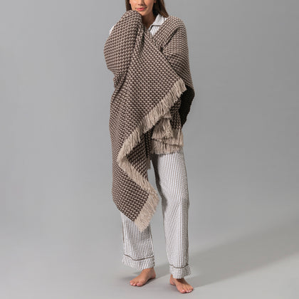 Model wearing a brown and ivory knit Cleo throw draped over her shoulders, with striped pajama pants.
