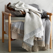 Ivory and gray Cleo knit throws with fringe, draped over a wood-framed armchair.