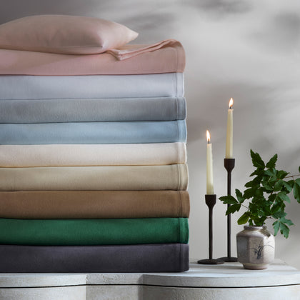 Dream Modal throws stacked in assorted colors, beside lit candles and a vase of greenery.