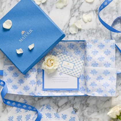 Matouk gift card in a blue gift box with patterned tissue paper and white rose petals