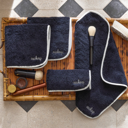Charcoal makeup towels embroidered makeup on a bamboo tray with a brush, lipstick, eyeshadow pot, and compact, diamond tile floor.