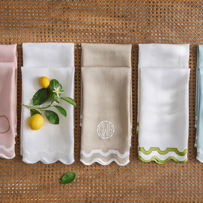 Guest towels in pink, white, tan monogrammed "SWB," green scalloped-edge, and light blue, laid on a woven surface with lemon branches.