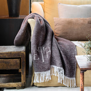 Same brown heathered Pezzo fringed throw with a monogram, draped over an armchair, shown from a wider angle.