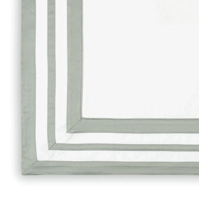 A close-up of a white tablecloth or napkin with a wide sage green border, showing the corner construction and double-stitched edges.