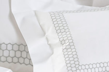 White bedding with a delicate gray geometric honeycomb pattern border on the pillowcases.
