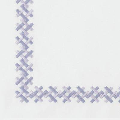 Close up of a napkin with a stitched geometric border in pale lavender and light blue