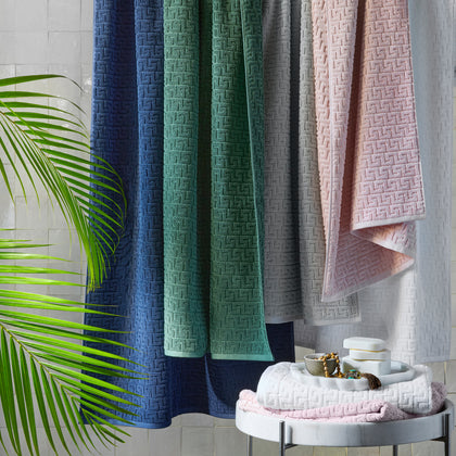 Athena greek-key textured towels in navy, green, gray, and pink, hung over a rail.