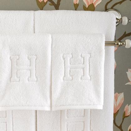 White Auberge towels with a monogrammed letter H in bold relief, hanging on a rod.