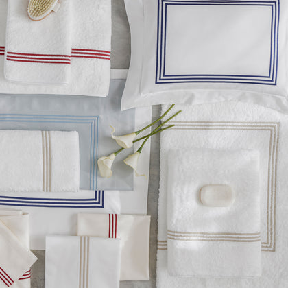 White Bel Tempo towels with striped trim in assorted colors, arranged flat with calla lilies and soap.