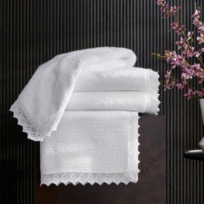 White Ellis lace-trimmed towels and bath mat, stacked.