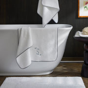 White Giza towels with charcoal monogram trim draped over a bathtub.