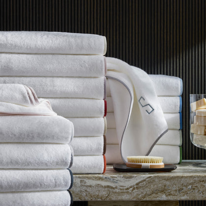 White Giza towels stacked with colorful edge trim, beside a monogrammed towel and bath brush.