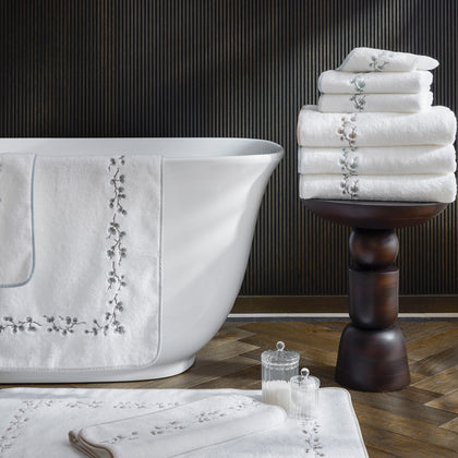 Jasmine Giza embroidered white towels draped on a bathtub with a matching bath mat