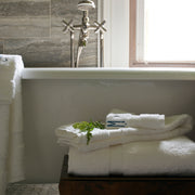 Ivory Lotus towels stacked beside a clawfoot tub, with a sprig of greenery.