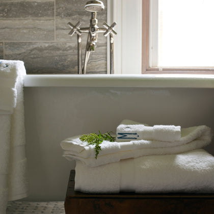 Ivory Lotus towels stacked beside a clawfoot tub, with a sprig of greenery.
