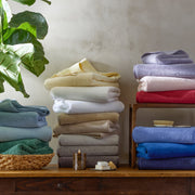 Milagro towels stacked in multiple colors on a wooden shelf.