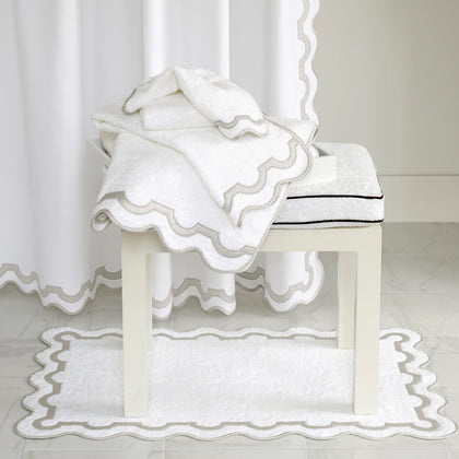 White Mirasol wavy-trimmed towels, bath mat, and shower curtain in a white bathroom.