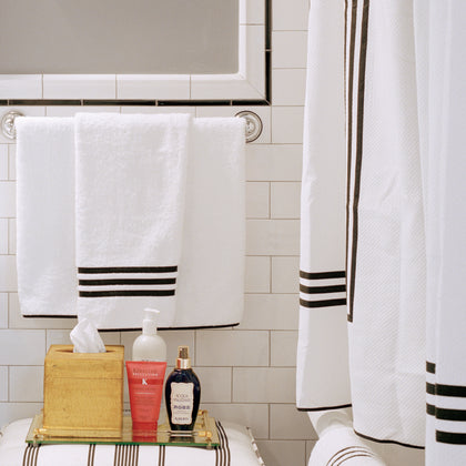 White Newport towels and shower curtain with black striped trim, styled in a tiled bathroom.