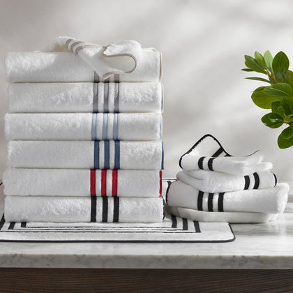 White Newport towels stacked with striped trim in assorted colors, on a marble table.