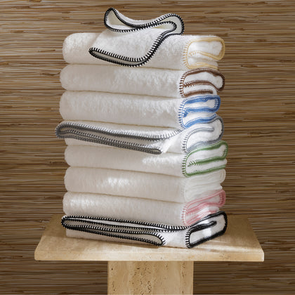 White Whipstitch towels with whipstitch trim in a rainbow of colors, stacked on a stone stand.