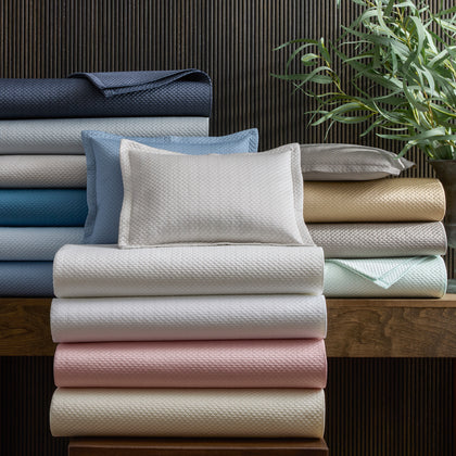 Alba textured pique bedding stacked in an array of pastel colors, near a potted plant.