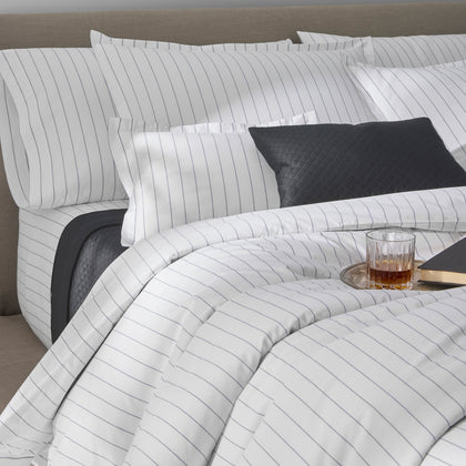 White and navy pinstripe Amalfi bedding with a charcoal quilted pillow, styled on a bed.