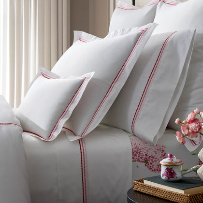 White bedding with triple-row embroidered dot borders in pink and red, a pink floral-print sheet, nightstand with a teacup and books.