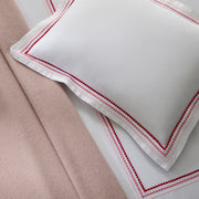 Close-up of white bedding with a triple-row embroidered dot border in pink and red, beside a solid blush wool blanket.