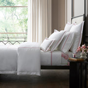 Amara Triple Pearl bedding in white with pink embroidered trim, styled on a bed.