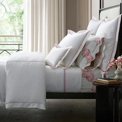Bed with white bedding and triple-row embroidered dot borders, a scalloped pink floral-print pillow, black metal frame, window with trees.