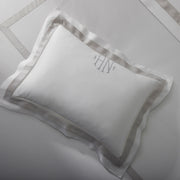 White Ambrose sham with tan satin border and monogram on a bed.