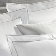 Close-up of Ansonia white pillow shams with grey tailored stitch trim.