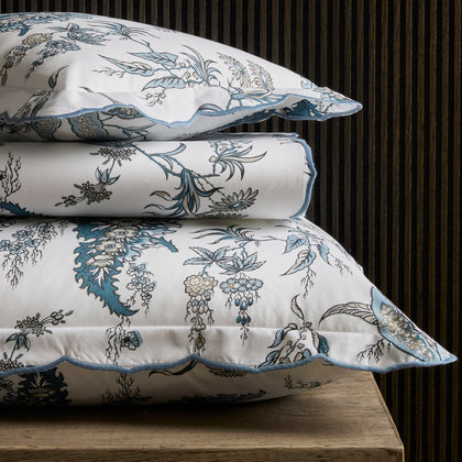 Blue Apolline floral print scalloped bedding, stacked on a wooden table.