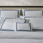 White AstorBraid pillow shams with navy looped-braid embroidered borders, styled with a plaid pillow sham on a bed with a dark wood headboard.