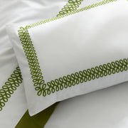 Close-up of a white AstorBraid pillow sham with green looped-braid embroidered borders, on a bed with a green bed skirt.
