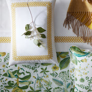 White AstorBraid sham with gold looped-braid embroidery, styled with a eucalyptus sprig, a mustard fringed throw, and green botanical-print bedding.