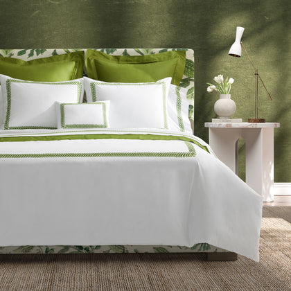 Bed with a botanical-print headboard dressed in white AstorBraid bedding with green looped-braid embroidery, by a marble nightstand with a lamp.