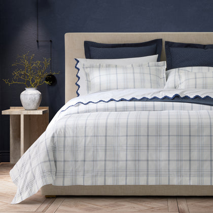 White and navy August Plaid bedding with scalloped trim, styled on a bed against a navy wall.