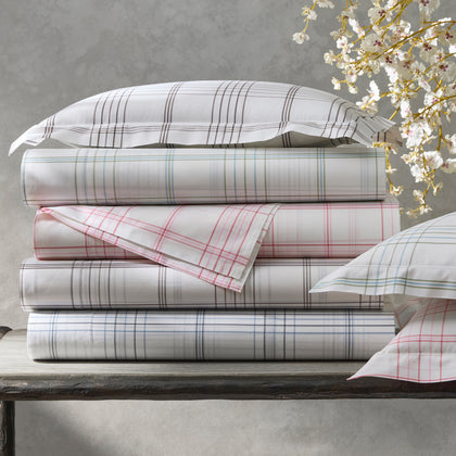 White August Plaid sheets in gray, green, pink, and blue, stacked beside cherry blossoms.