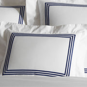 Close-up of stacked white BelTempo pillow shams with triple navy line embroidered borders.